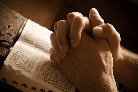 Hands closed in prayer on an open bible